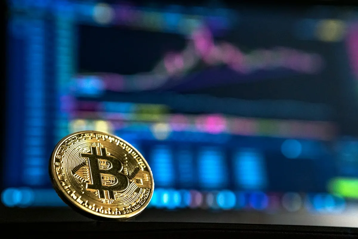 Arka planda finansal grafiklerin bulunduğu altın renkli bitcoin madeni parası (temsili fotoğraf)